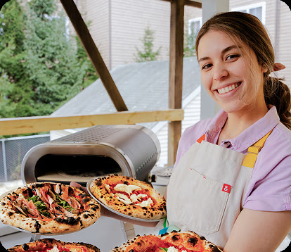 A local baker smiling while presenting freshly made pizzas